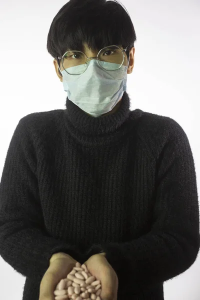Kinesisk kille i medicinsk mask med en handfull piller. Covid-2019. Vit bakgrund — Stockfoto