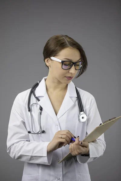 Schöne Ärztin schaut auf Klemmbrett mit Patienten Diagnose, grauer Hintergrund — Stockfoto