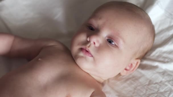 Spädbarn bebis ligger på blöja på sängen, flyttar händerna, ler och försöker prata — Stockvideo