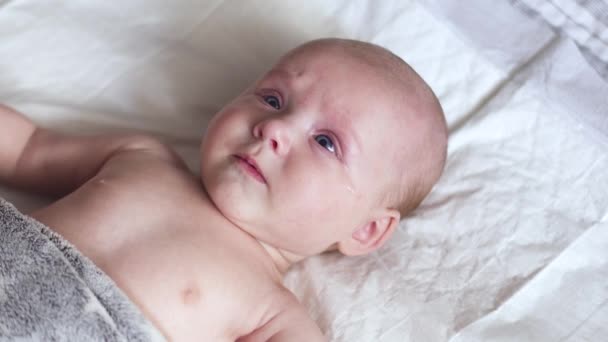 Pasgeboren baby ligt op luier op bed, beweegt zijn handen, glimlacht en probeert te praten — Stockvideo