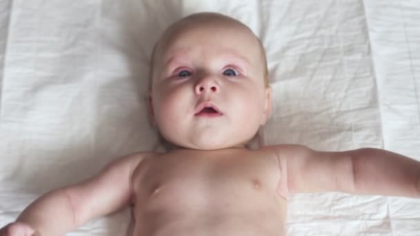 Счастливый новорожденный малыш на кровати, двигает руками, улыбается, пытается говорить, материнство — стоковое видео