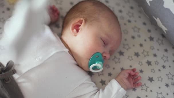 Um bebê recém-nascido dorme em um berço com uma chupeta azul na boca — Vídeo de Stock
