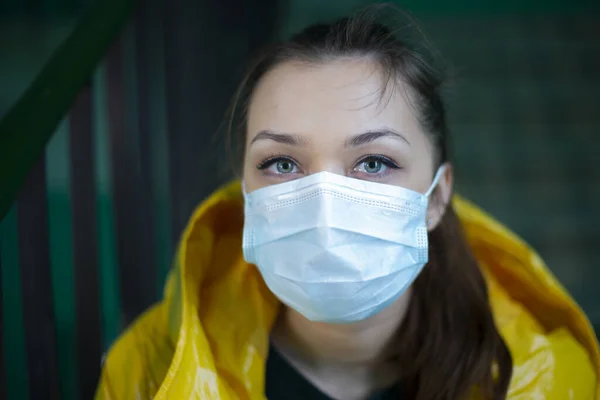 Una chica caucásica con máscara médica en la cara y con una chaqueta de color amarillo brillante — Foto de Stock