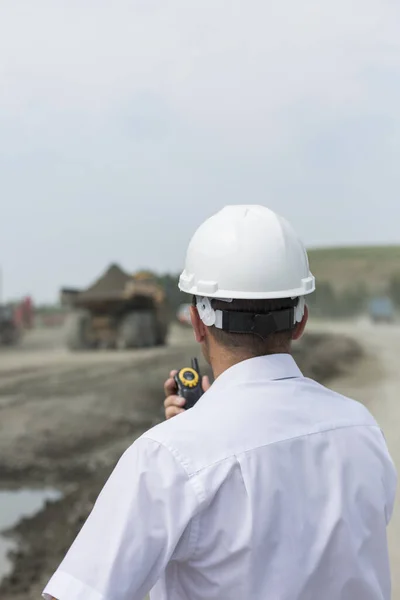 Důlní inženýr v bílé košili a helmě dohlíží na řízení terénních vozů v lomu — Stock fotografie