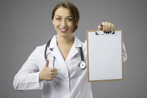 Mooie vrouwelijke arts met blanco klembord tonen als teken, kopiëren ruimte — Stockfoto