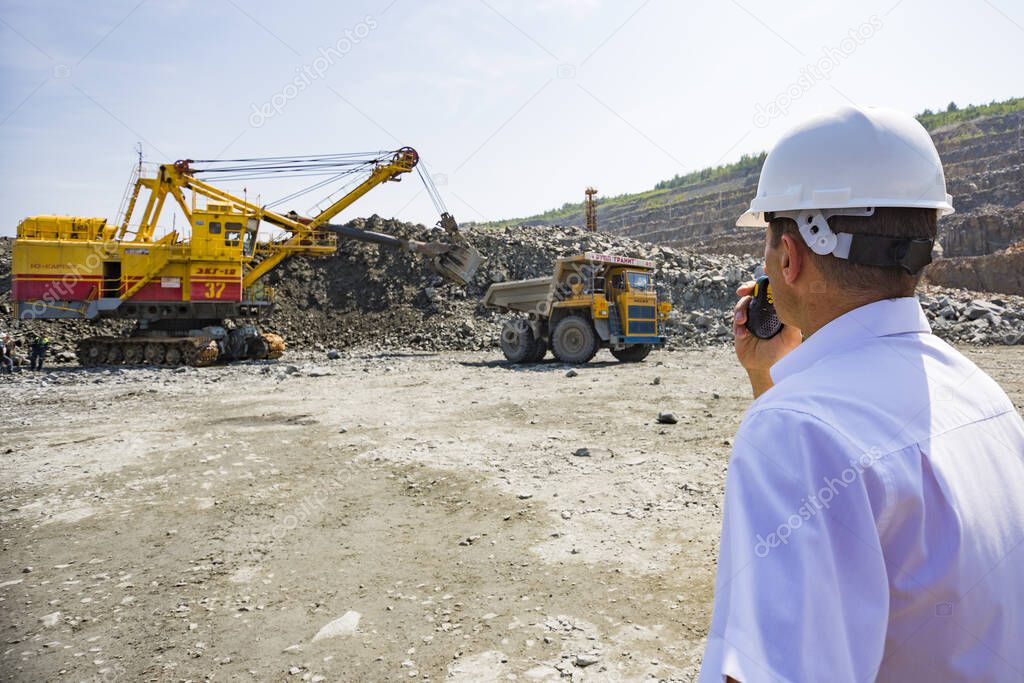 Mining engineer in white shirt helmet supervises loading dumpers granite quarry
