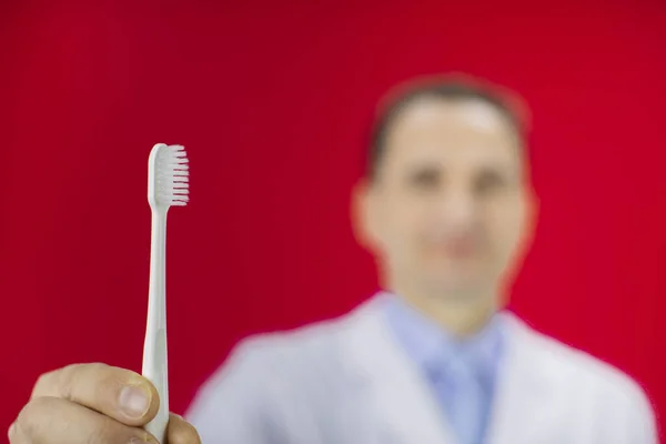 Volwassen tandarts man houdt tandenborstel geïsoleerde rode achtergrond. Close-up tand. — Stockfoto
