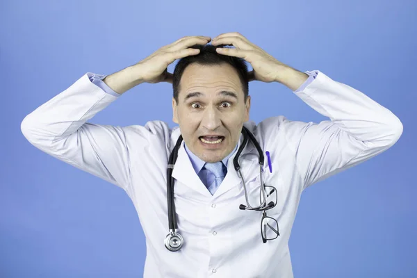 Doctor conmocionado gritando de miedo con la mano levantada en la cabeza sobre el fondo azul — Foto de Stock