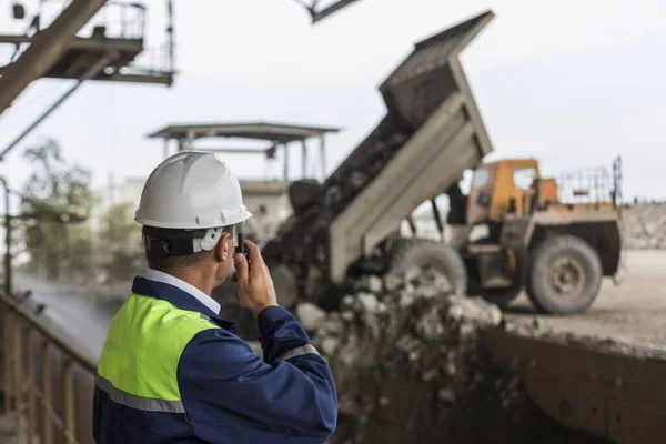 Důlní inženýr ve žlutomodré uniformě a helmě dohlíží na vykládání kontejnerů — Stock fotografie