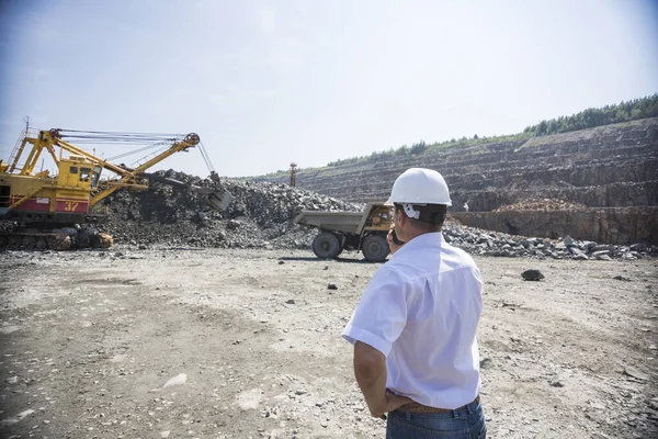Důlní inženýr v bílé košili a helmě dohlíží na nakládku kontejnerů v lomu — Stock fotografie