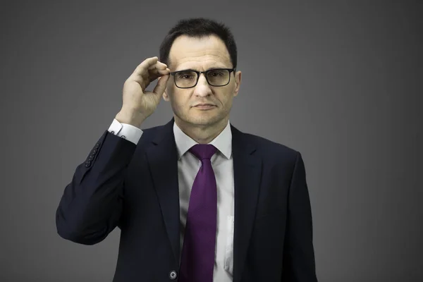 Уверенный сексуальный мужчина бизнесмен в официальном костюме держит очки, серый фон — стоковое фото