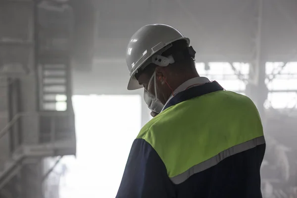 Důlní inženýr v bílé helmě a respirátoru kontroluje zaprášenou špinavou dílnu — Stock fotografie