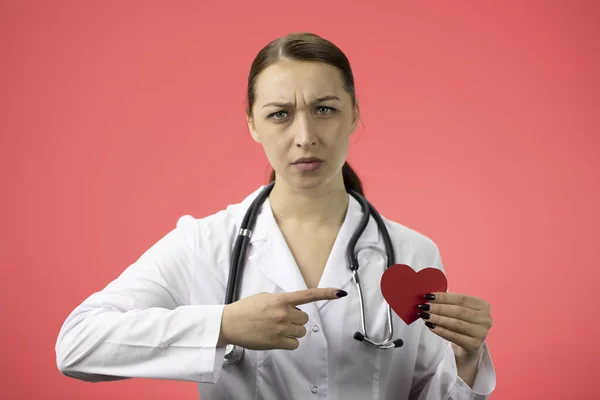 Beautiful dissatisfied doctor pointing on red paper heart in hand, heart attack — Stock Photo, Image