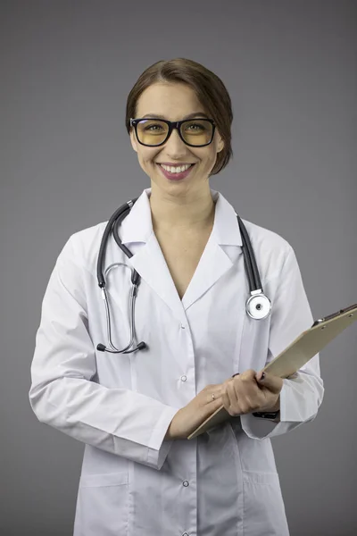 Netter Arzt im weißen Kittel, Stethoskop mit Klemmbrett, freundliche Blicke in die Kamera — Stockfoto