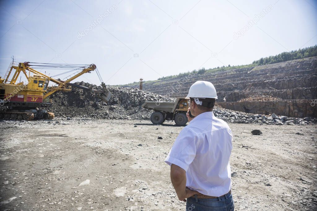 Mining engineer in white shirt and helmet supervises loading dumpers in quarry