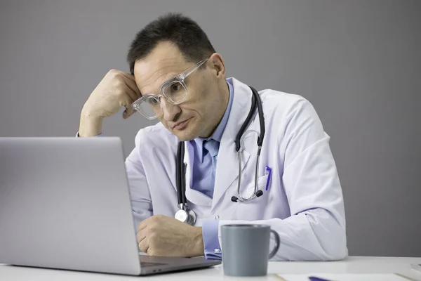 Médecin travaillant au bureau sur son ordinateur portable avec une casquette de café . — Photo