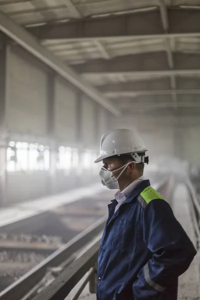 Důlní inženýr v bílé helmě a respirátoru kontroluje zaprášenou špinavou dílnu — Stock fotografie