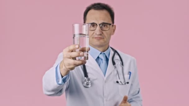 Médico de mediana edad iholds vaso de agua limpia y muestra como signo con el pulgar hacia arriba — Vídeo de stock