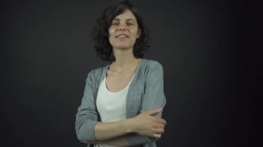 Gri kazağın altındaki beyaz elbiseli genç kadın gülümseyerek poz veriyor.