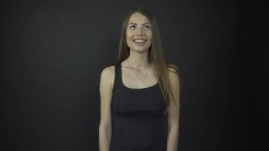 Siyah elbiseli uzun saçlı esmer sahnede konuşuyor ve gülüyor.