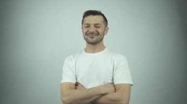 Tişörtlü neşeli adam gülüyor ve yüzünü elinin arkasına saklıyor.