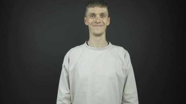 Красивый парень в сером свитере улыбается и пожимает руку — стоковое видео