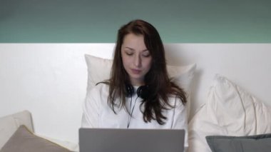 Yatakta uzun saçlı, laptopla çalışan güzel, beyaz bir kadın..