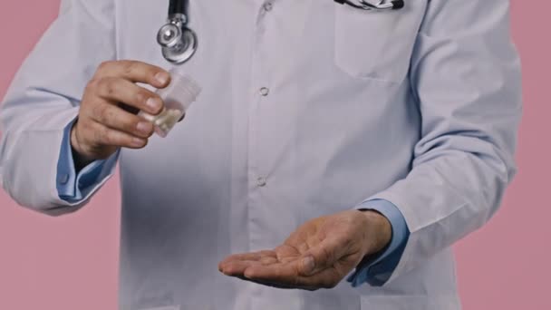 Close up view of doctor pouring pills into palm of his hand on pink background — Stock Video