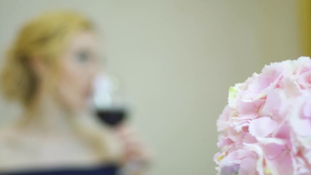 Mulher branca espera em uma mesa de parceiros para uma data e bebe vinho tinto — Vídeo de Stock