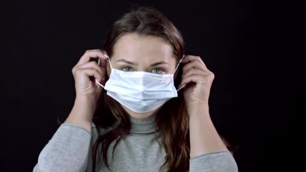 Schöne Frau setzt medizinische Maske auf. Schwarzer Hintergrund. Weltweite Pandemie-Covid-19 — Stockvideo