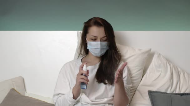 Fille effrayée masque de protection, pyjama dans le lit à la maison pulvérisation antiseptique sur la main — Video