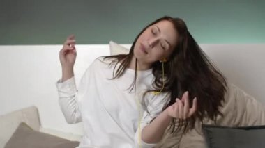 Sarı kulaklıklı yakışıklı kız evde yatakta müzik dinliyor ve gülüyor.