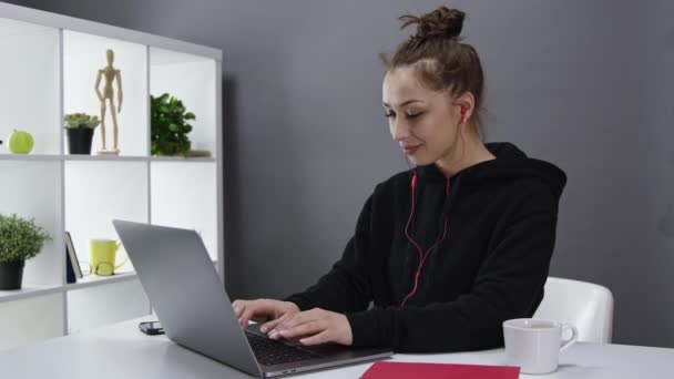 Attrayant freelance féminine avec écouteurs fonctionne à l'ordinateur portable, parler sur webcam — Video