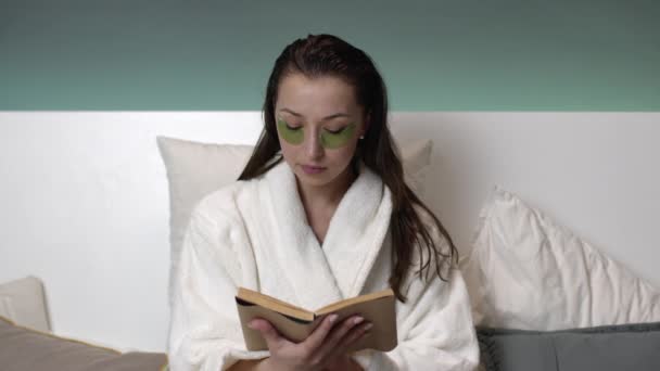 Mujer sexy en abrigo blanco con parches en la cara lee libro antes de ir a la cama — Vídeos de Stock