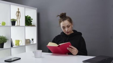 Siyah kapüşonlu güzel kız ilginç bir şekilde evde kitap okuyor ve gülümsüyor..