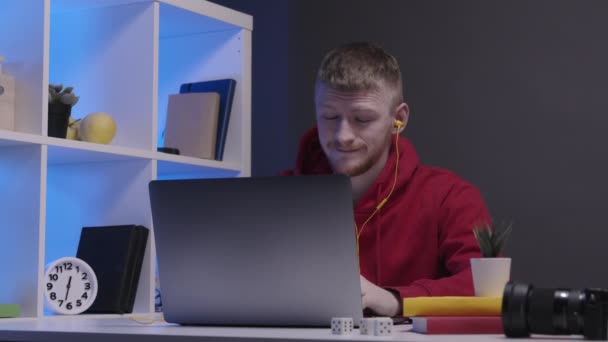 Cansado hombre atractivo freelancer con auriculares trabajando en el ordenador portátil hasta tarde por la noche — Vídeo de stock