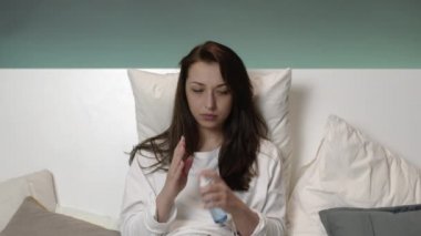 Evde pijamalı, yatakta korkmuş genç bir kız her yere antiseptik serpiyor..