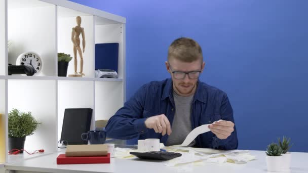 Blanke man met baard in een jeans shirt overweegt onkosten en plant een budget. — Stockvideo