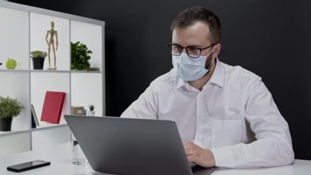 Schöner Geschäftsmann in Schutzmaske arbeitet in Quarantäne am Laptop — Stockvideo