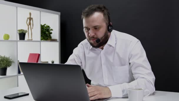 Jovem homem zangado em terno formal e fones de ouvido trabalhando longe do escritório no laptop — Vídeo de Stock