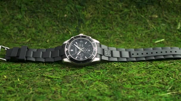 Ібах, Швейцарія 7.04.2020 - Вікторінокс Людина спостерігає за чорним годинником з нержавіючої сталі, який лежить на зеленому моху. — стокове відео