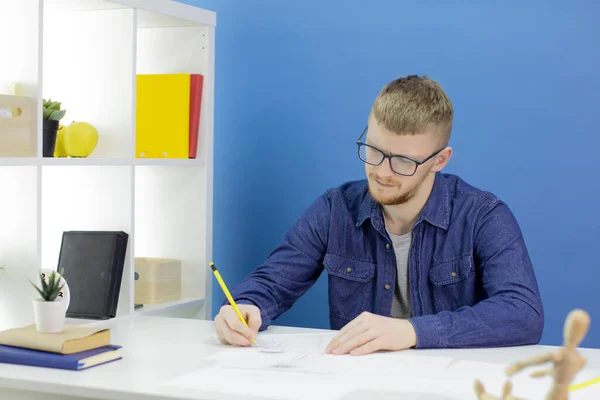 Pensativo joven diseñador enfocado dibuja con lápiz en el estudio con maniquí de madera — Foto de Stock