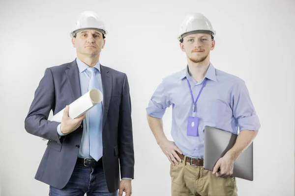 Dos ingenieros miran con confianza a la cámara con sonrisa, sujetando el portátil y dibujando —  Fotos de Stock