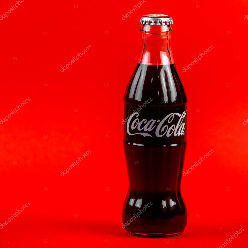 Atlanta, Georgia, USA April 1, 2020: closeup of classic contour glass bottle of Coca Cola white logo from USA isolated on red background. concept of globalism, global brand, worldwide spread.