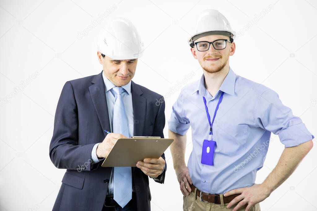 Two engineers different ages look at camera smiling, making notes on clipboard