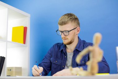 Düşünceli odaklı genç tasarımcı stüdyoda ahşap kuklayla kalem çiziyor.