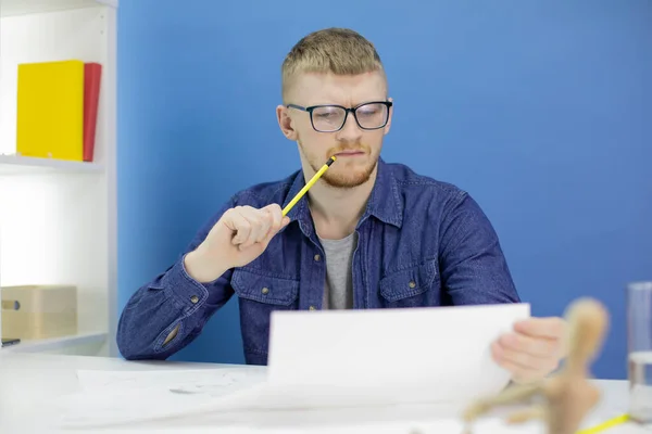 Pensativo joven diseñador enfocado dibuja con lápiz en el estudio con maniquí de madera — Foto de Stock