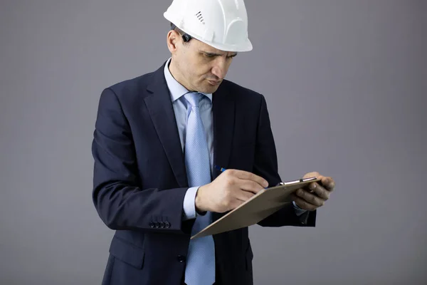 Construtor preocupado em capacete branco e roupas formais escreve na área de transferência — Fotografia de Stock