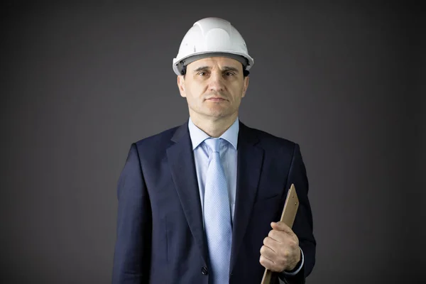 Уверенный в себе инженер в шлеме и формальной одежде держит буфер обмена смотрит в камеру — стоковое фото