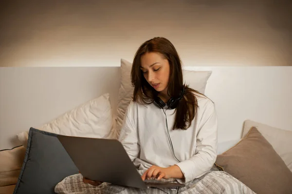 Joven chica sexy en ropa casual sentado en la cama, trabajando en el ordenador portátil desde casa — Foto de Stock